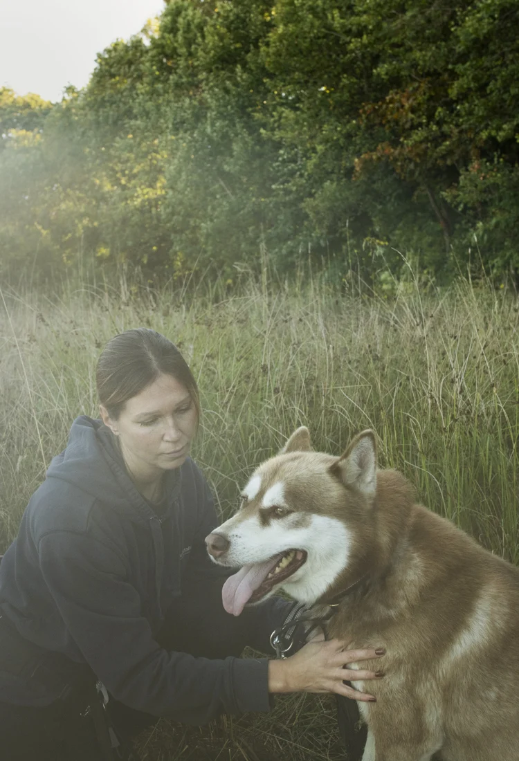 En kvinna som knäböjer bredvid en brun och vit hund.